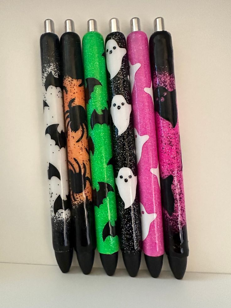 five different colored pens lined up next to each other on a white surface with black and green designs