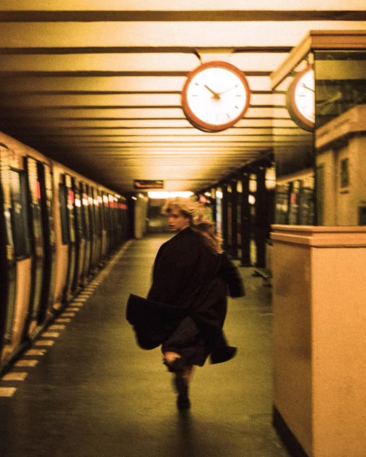 a woman walking down a train station next to a clock