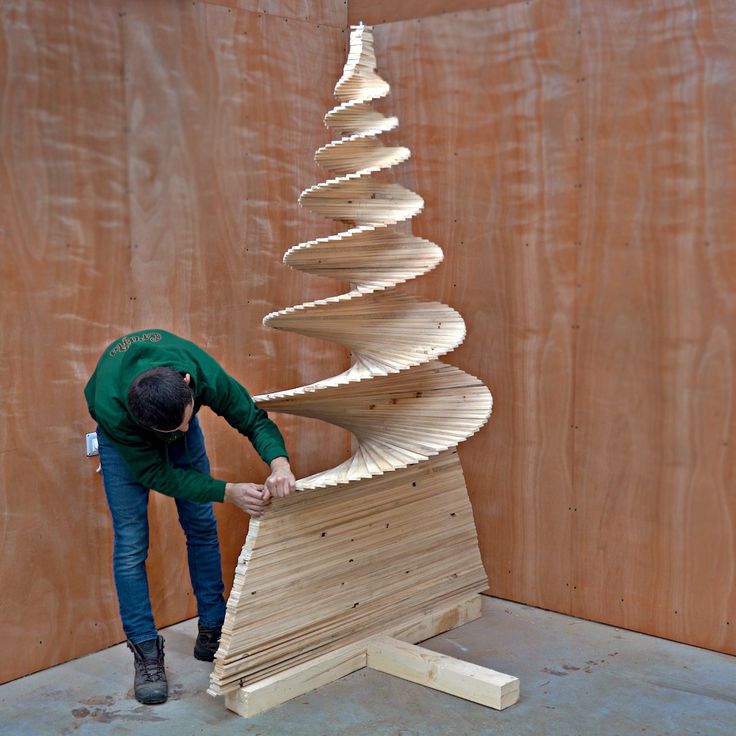 a man standing next to a wooden christmas tree on top of plywood planks