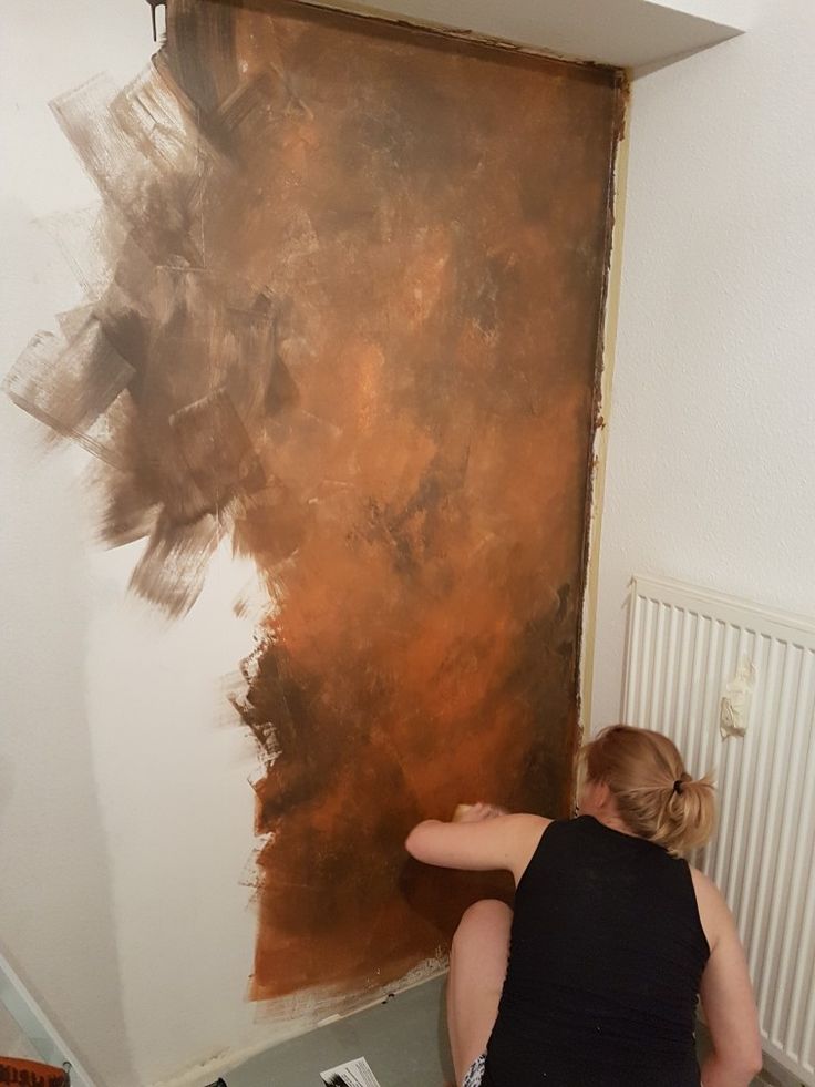 a woman sitting on the floor in front of a wall painting with brown and black colors