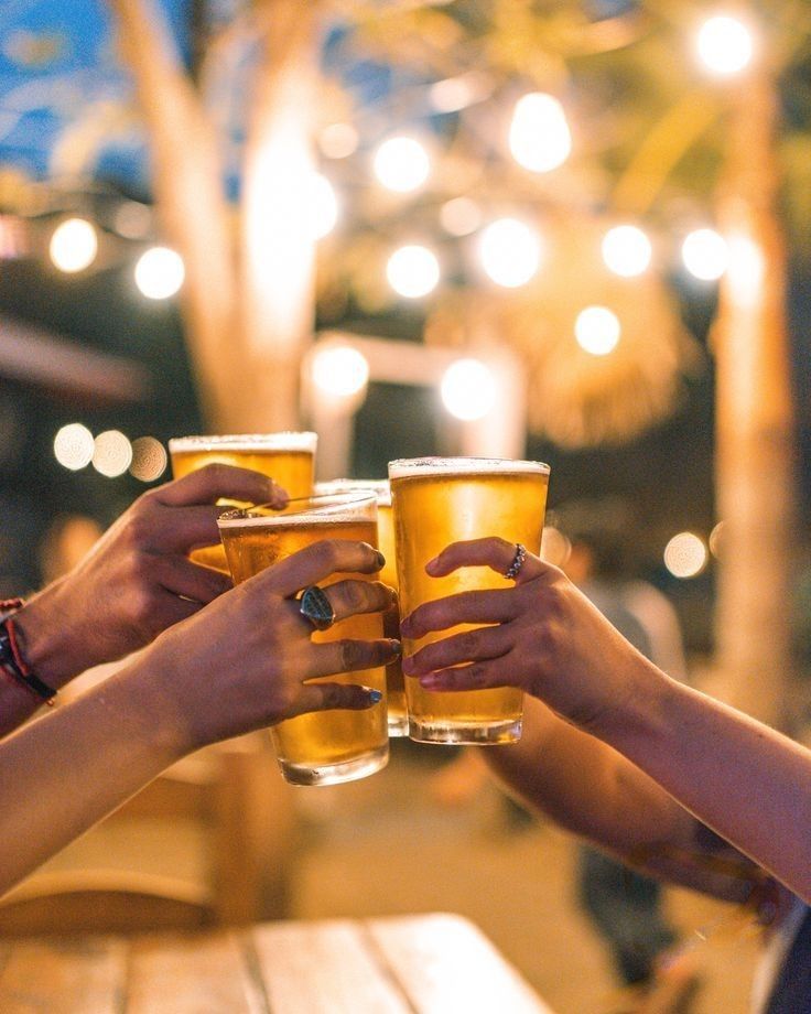 two people toasting with beer glasses in front of them on a wooden table outside