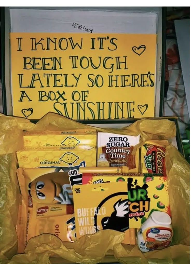 an open yellow bag filled with snacks and other items next to a sign that says i know it's been tough lately so there is a box of sunshine