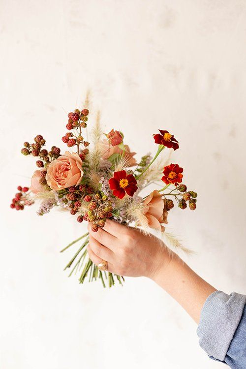 a person holding a bunch of flowers in their hand with white wall and background behind them