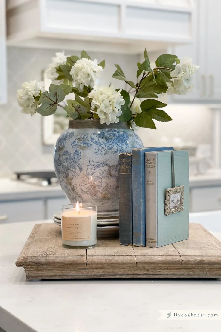 a blue and white vase filled with flowers on top of a wooden tray next to two books