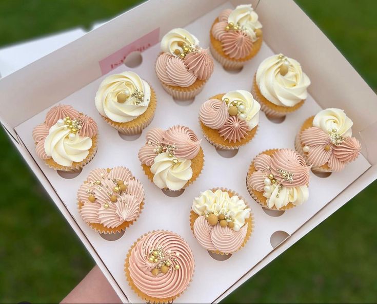 a box filled with pink and white cupcakes on top of a green field