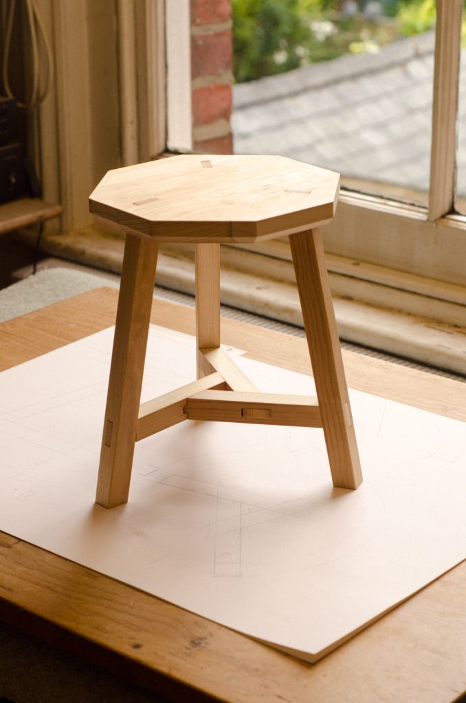 a small wooden stool sitting on top of a white mat in front of a window