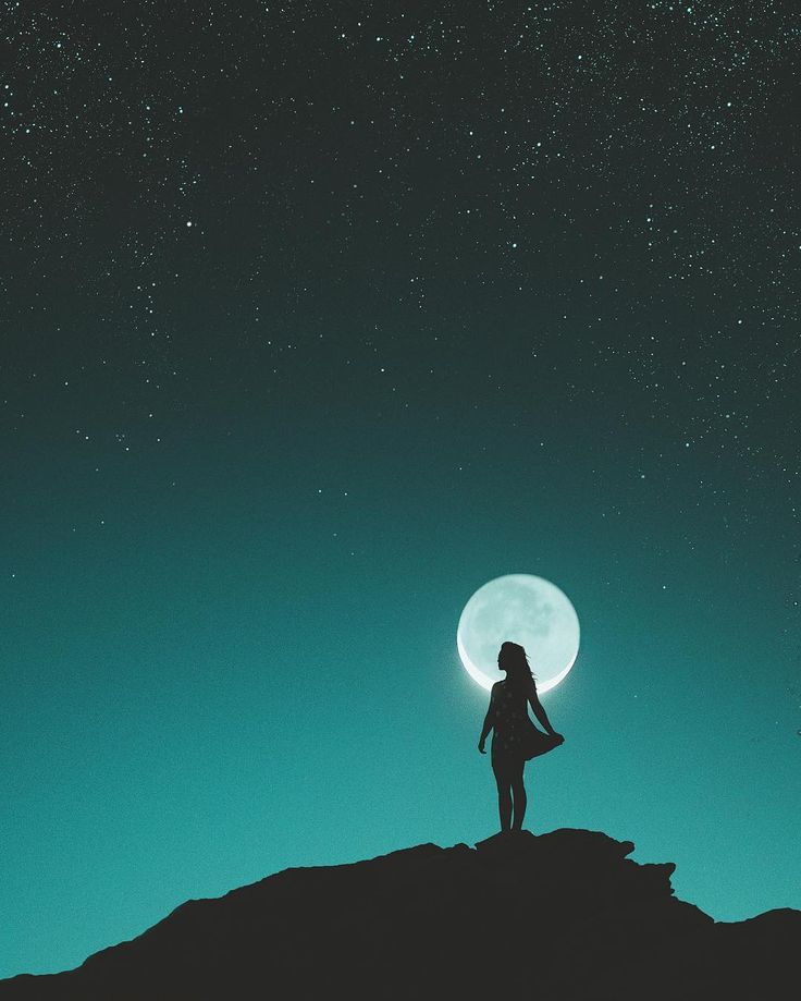 a woman standing on top of a hill under a full moon