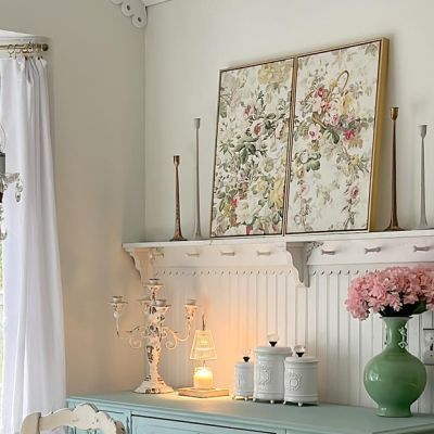 a blue dresser with flowers and candles on it in a white room next to a window