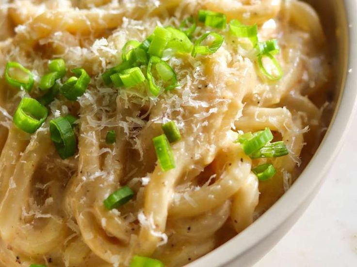 a white bowl filled with pasta covered in cheese and scalloped green onion sprinkles