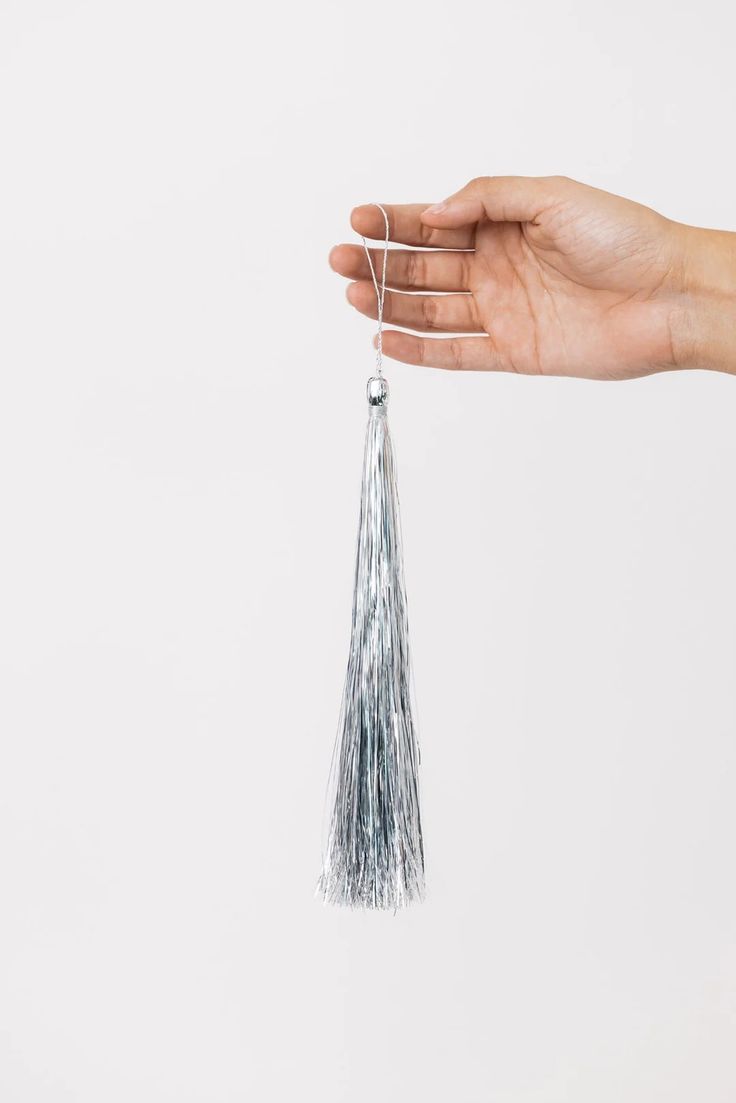 a person's hand holding a silver tassel on a white background with the string attached to it