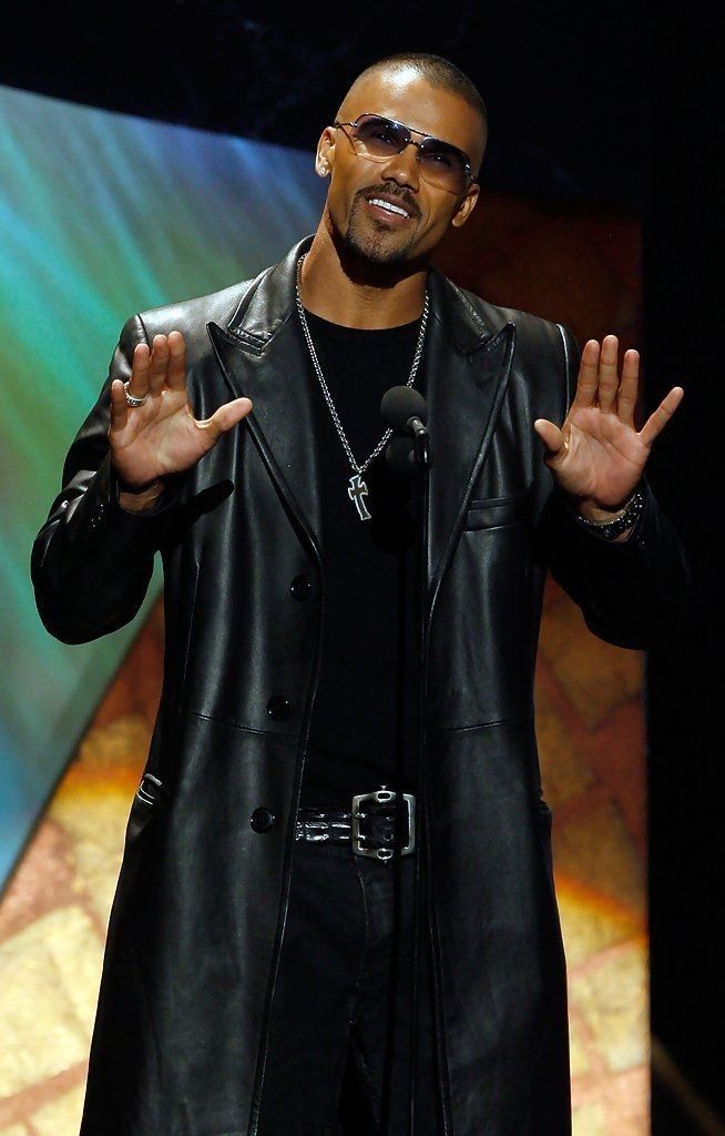 a man in black jacket and sunglasses standing on stage with his hands out to the side