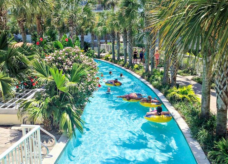 people are floating down the lazy waterslide at an outdoor swimming pool with palm trees