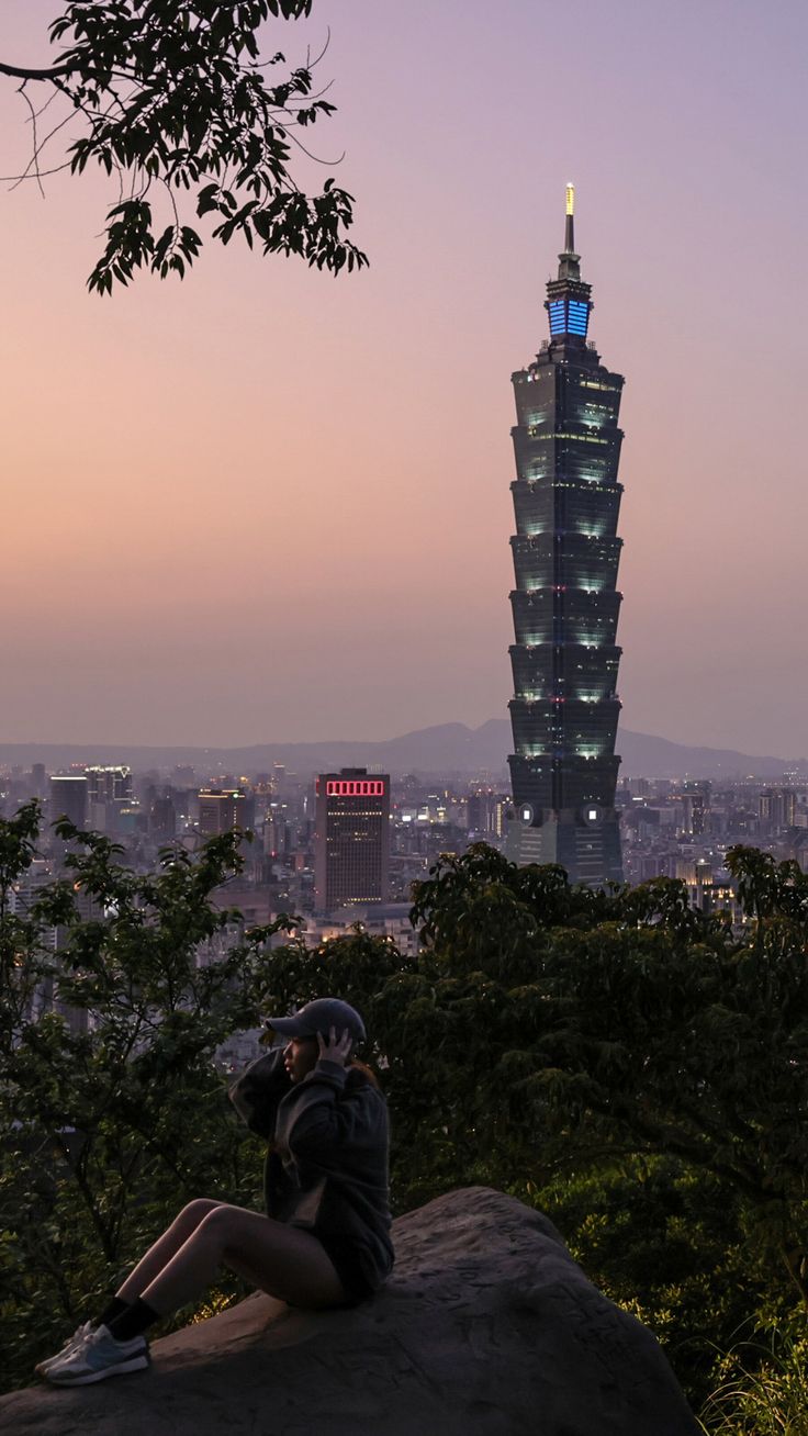 a person sitting on top of a rock with a view of the city in the background