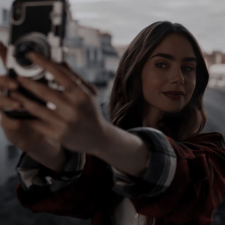 a woman taking a selfie with her cell phone in front of the ocean and buildings