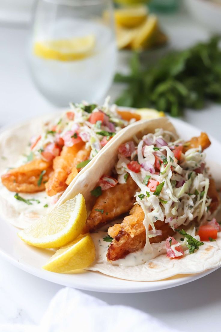 two fish tacos with cole slaw and lemon wedges on a white plate