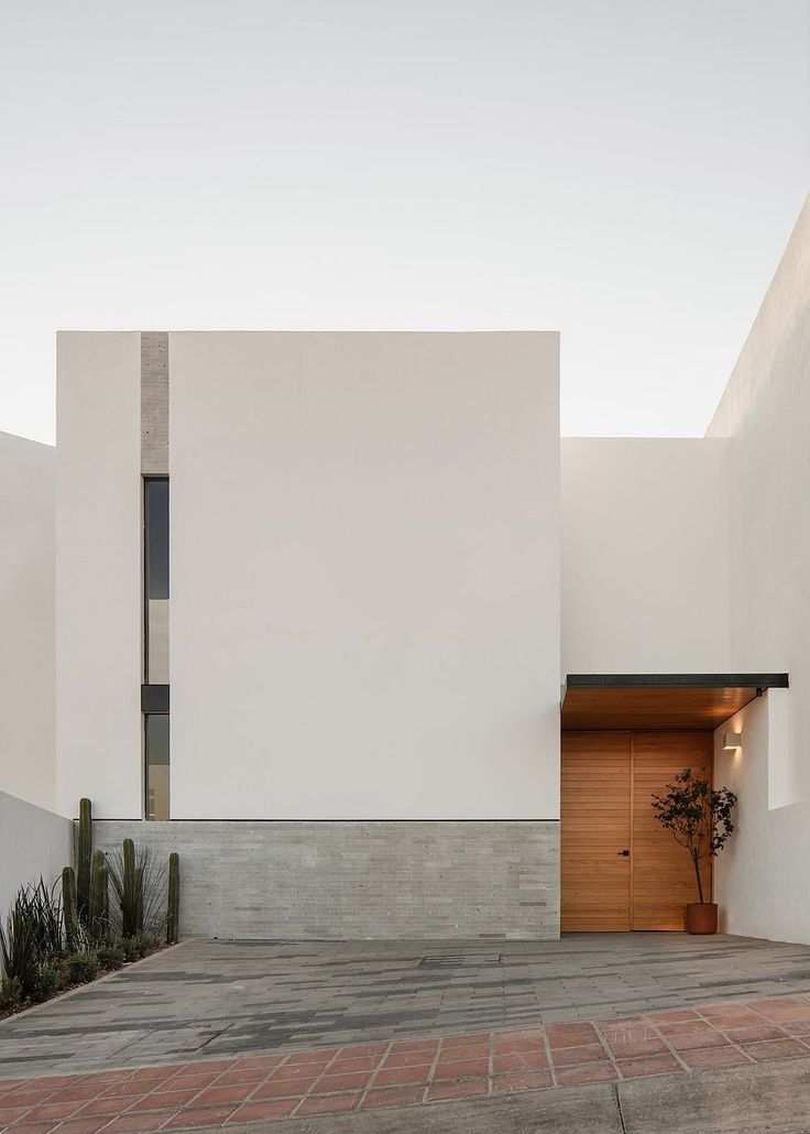 an entrance to a white building with cactus in the foreground and brick walkway leading up to it