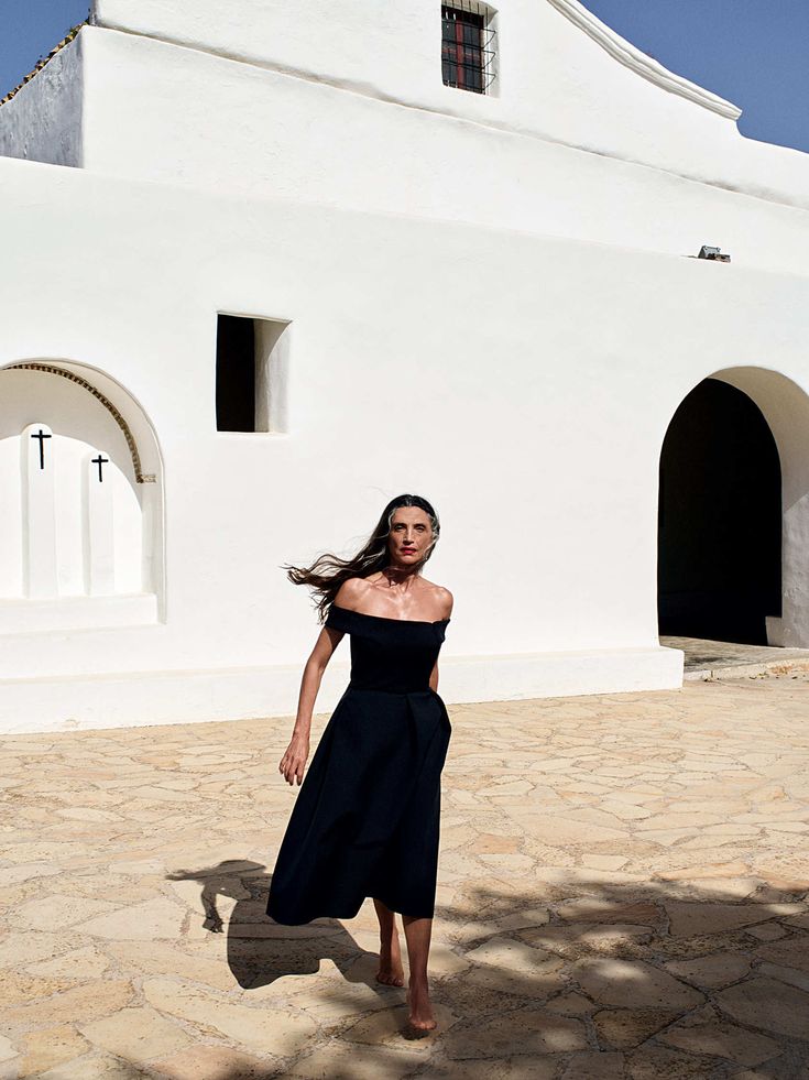 a woman standing in front of a white church with her hair blowing in the wind