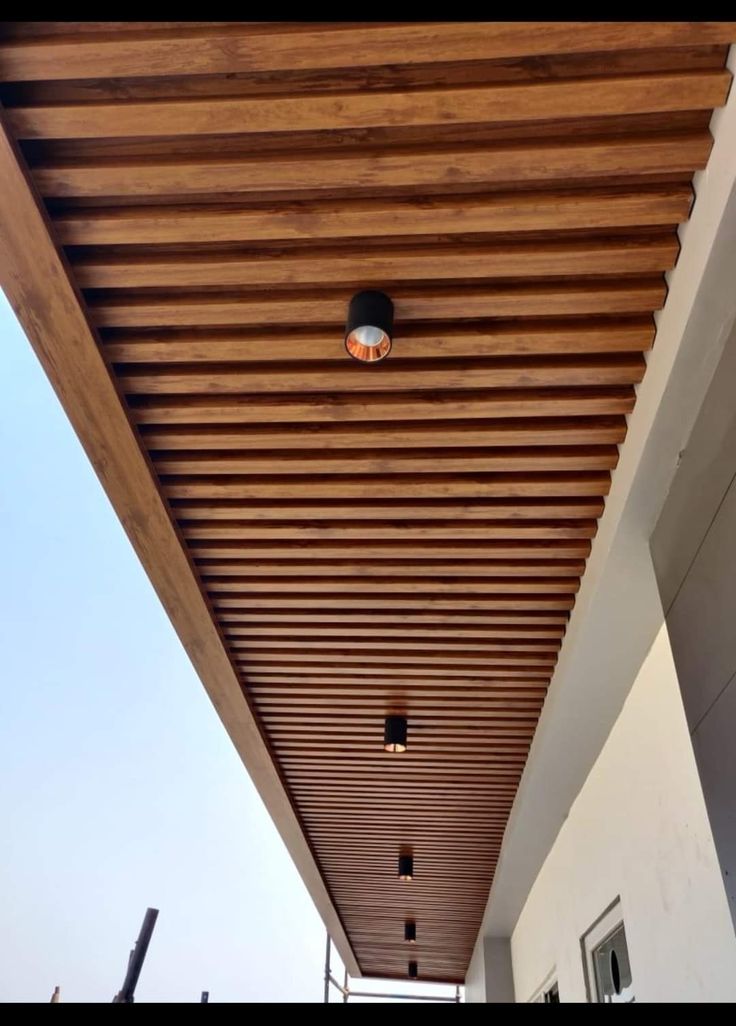 an outdoor patio with wooden slatted ceiling and lights on the outside side of the house