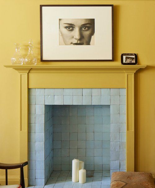 a fireplace in a living room with yellow walls and blue tiles on the mantel