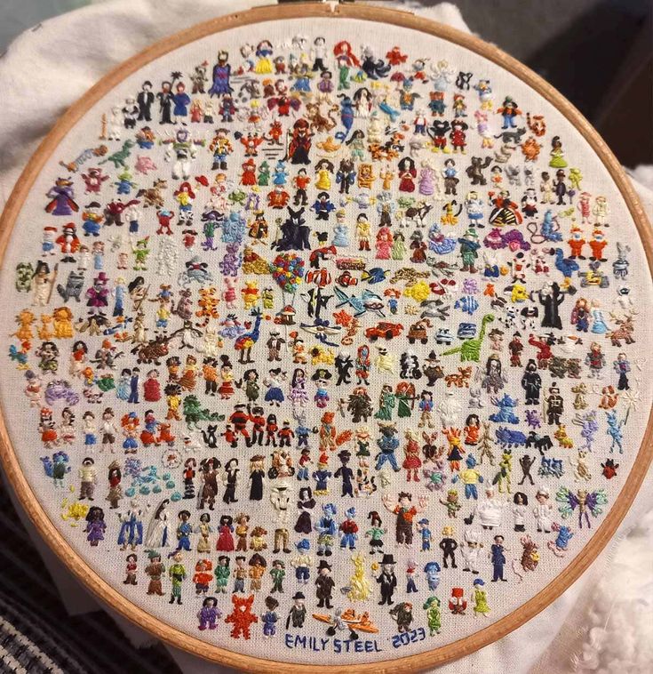 a cross stitch pattern with people all over it on a piece of white fabric next to a pair of scissors