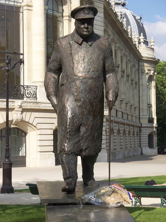 a statue of a man with a hat and cane standing in front of a building