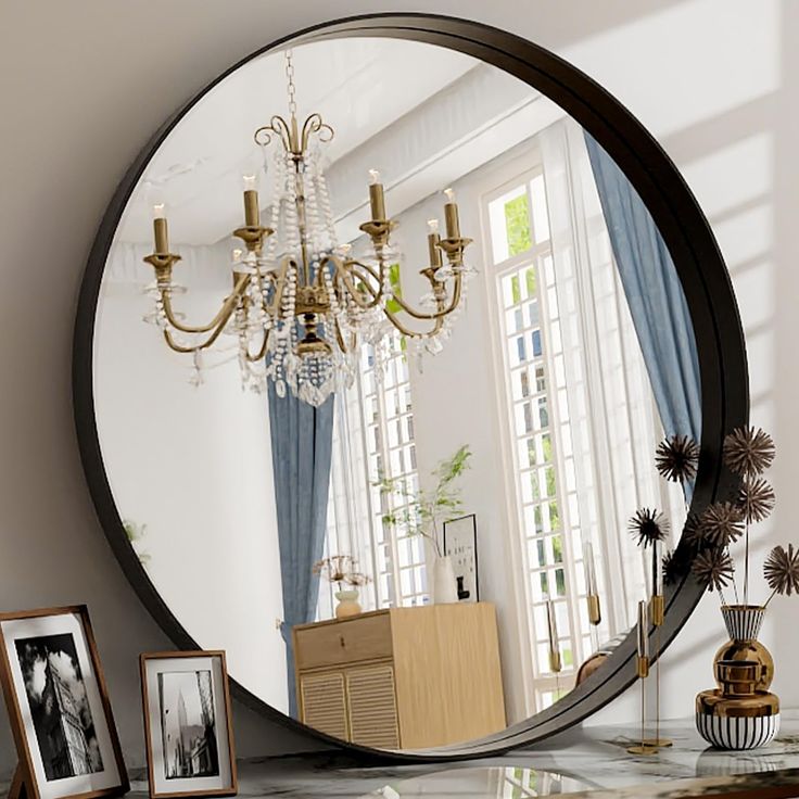 a large round mirror sitting on top of a table next to a vase and pictures