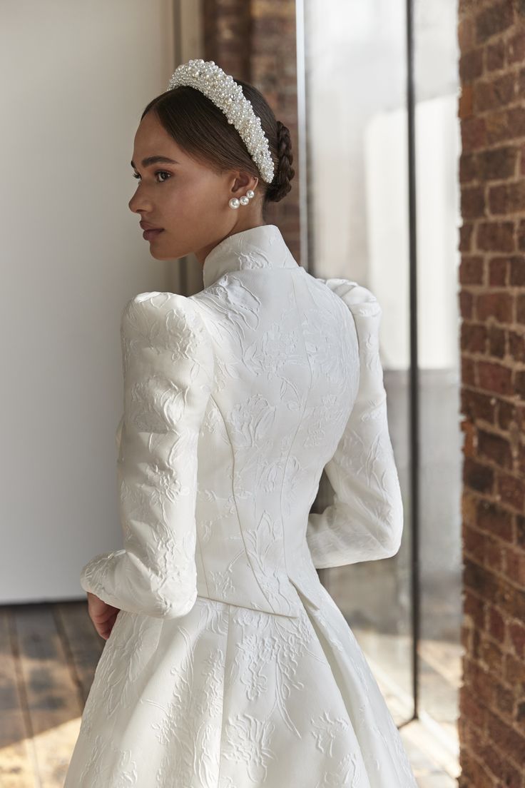 a woman in a white wedding dress standing next to a brick wall