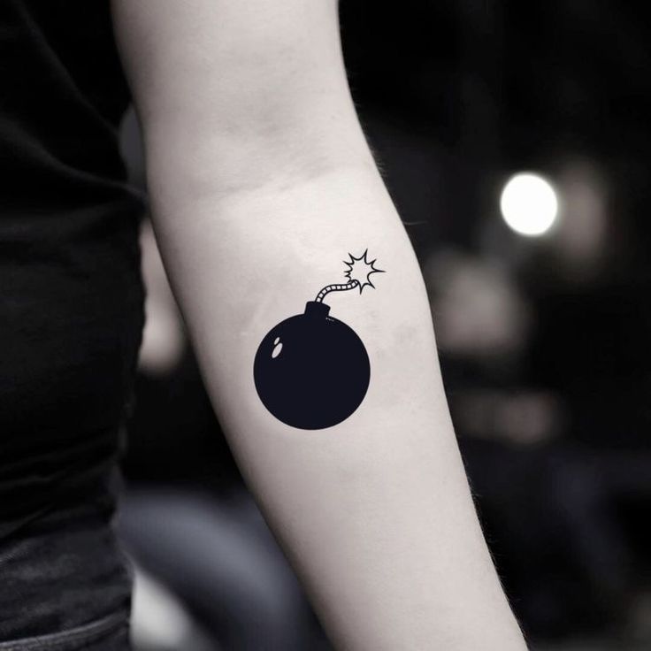 a woman's arm with a small black bomb tattoo on the left inner arm