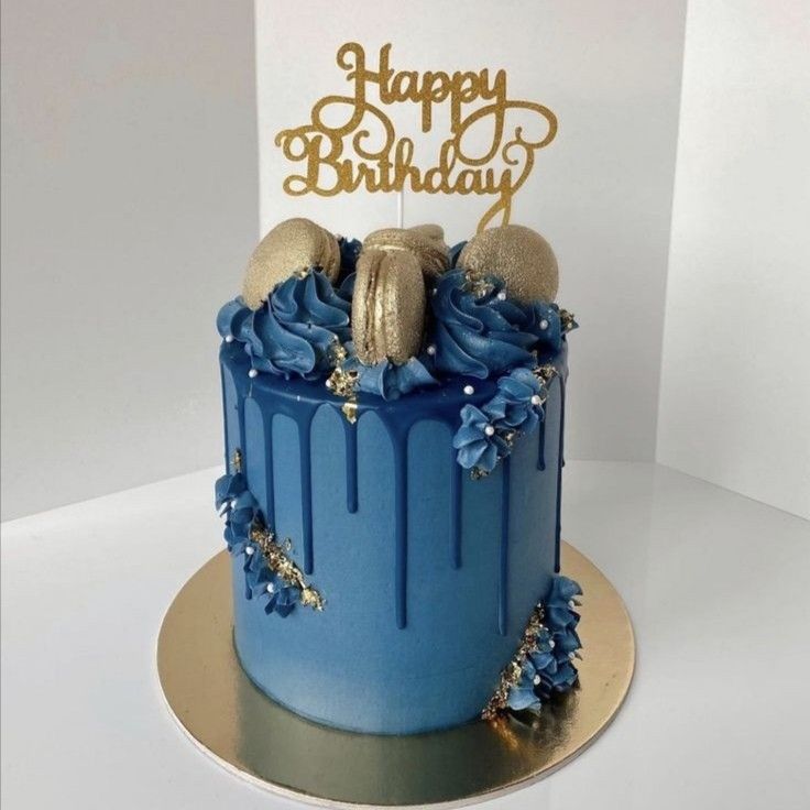 a birthday cake with blue frosting and gold decorations on top, sitting on a white table