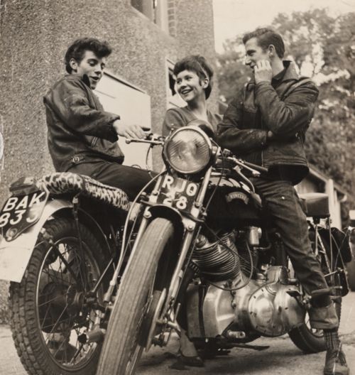 three men sitting on a motorcycle talking to each other while one man talks on the phone