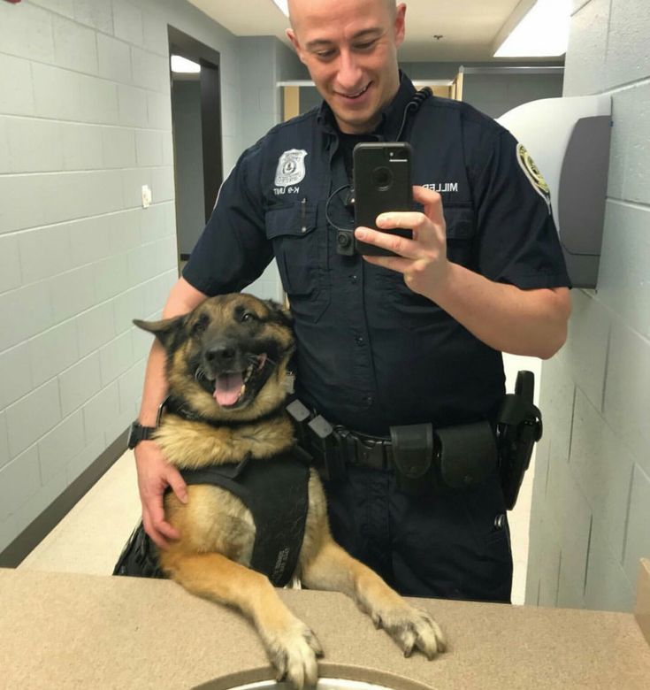 a police officer taking a selfie with his german shepard dog in the bathroom sink