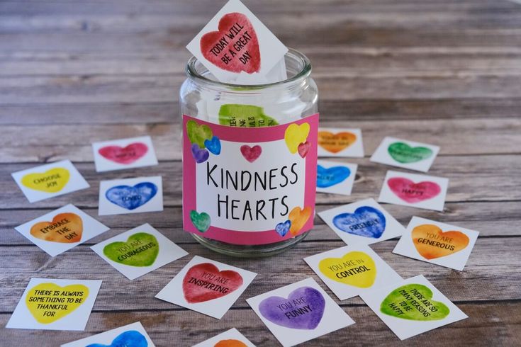 a jar filled with heart shaped stickers sitting on top of a wooden table next to hearts