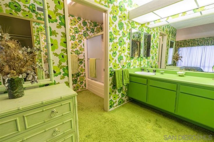 a green bathroom with floral wallpaper and drawers