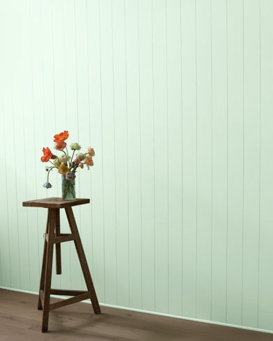 a small wooden table with flowers on it in front of a green wall and wood floor