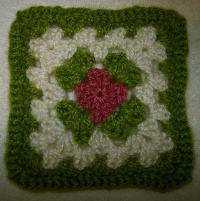 a crocheted square with a red flower on the center and green leaves in the middle