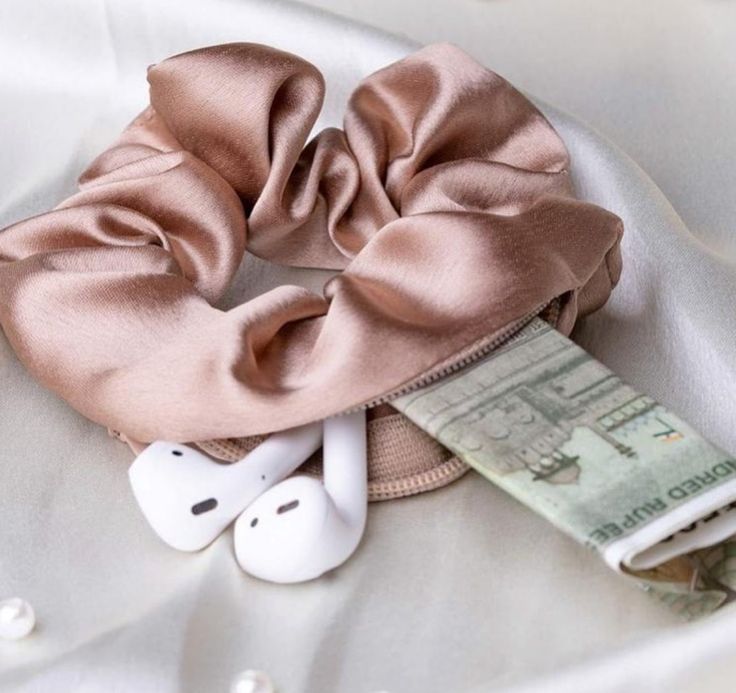 a pink scrunffle on top of a white satin material with headphones and money