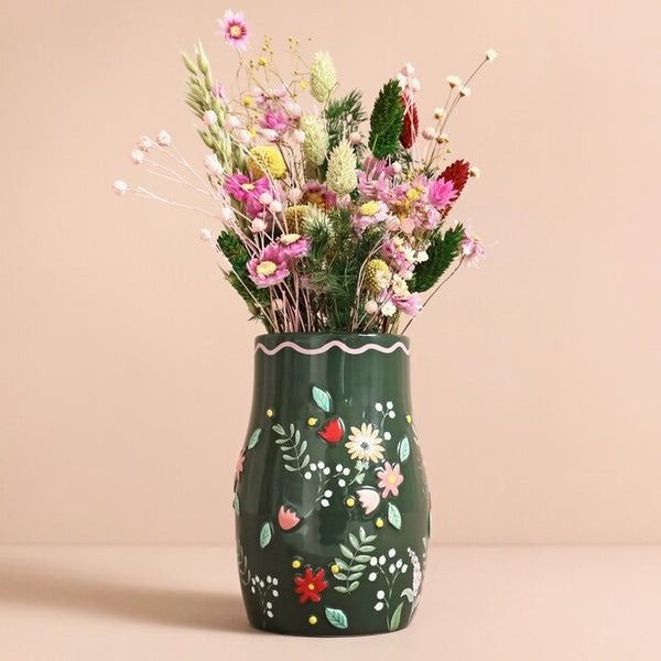 a green vase filled with lots of flowers on top of a white tablecloth covered floor