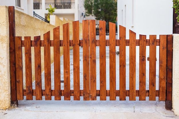 a wooden gate is shown in front of a white building and some plants on the sidewalk