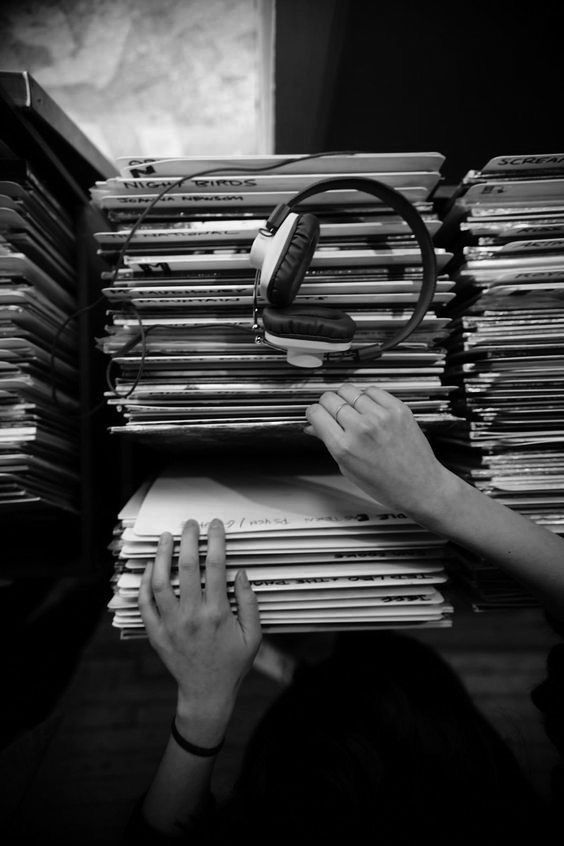 a person with headphones on is reading a book next to a stack of records