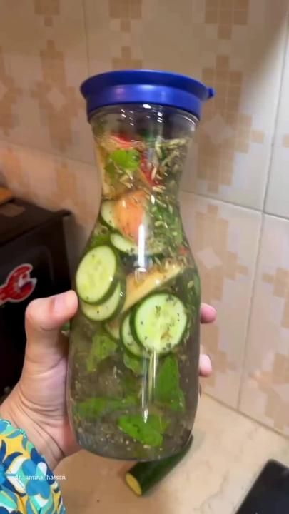 a person holding up a jar filled with cucumbers and other veggies