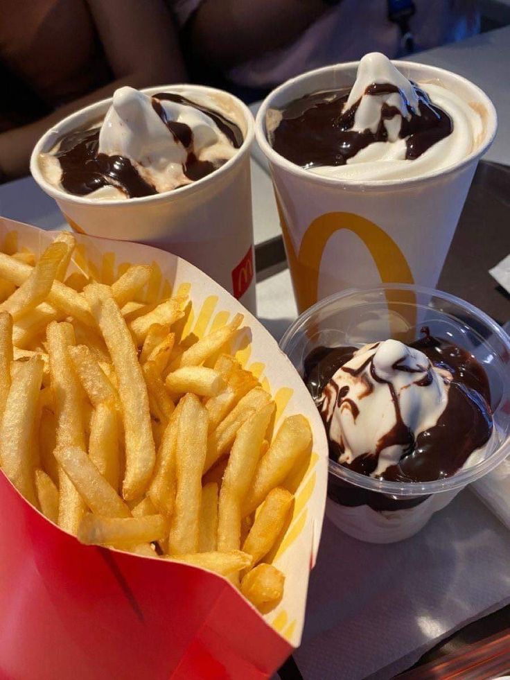 three cups of ice cream, chocolate sauce and french fries on a tray at a restaurant