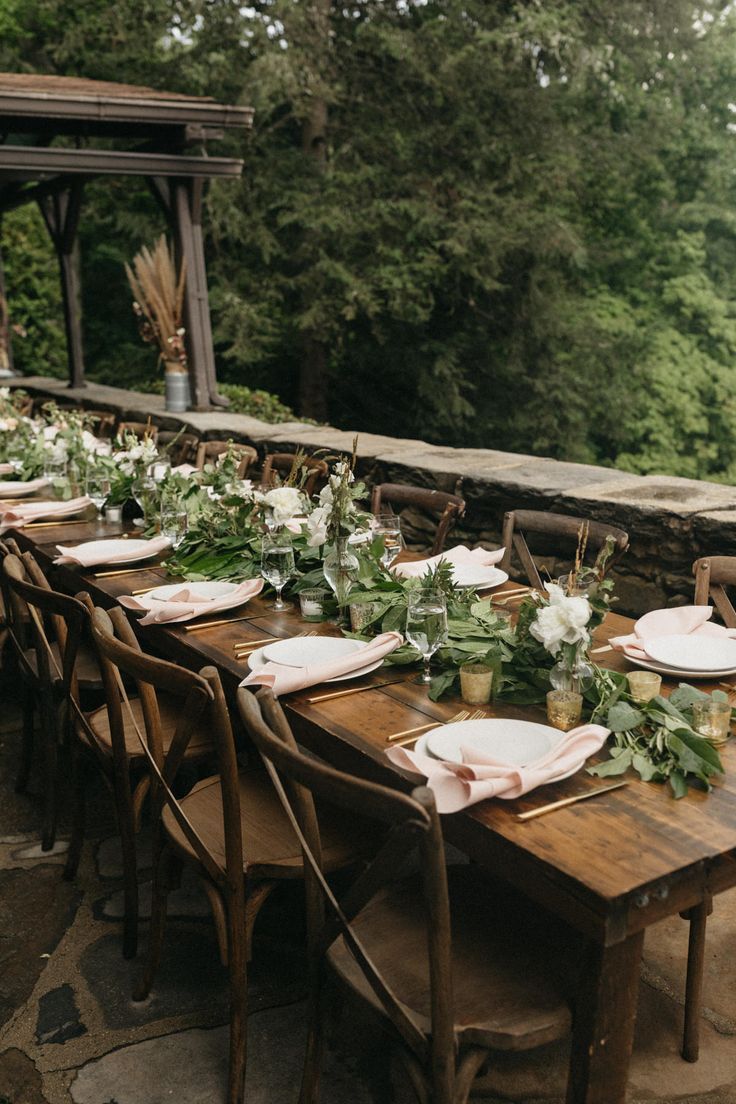 a long table set with plates and place settings for an outdoor wedding reception in the woods