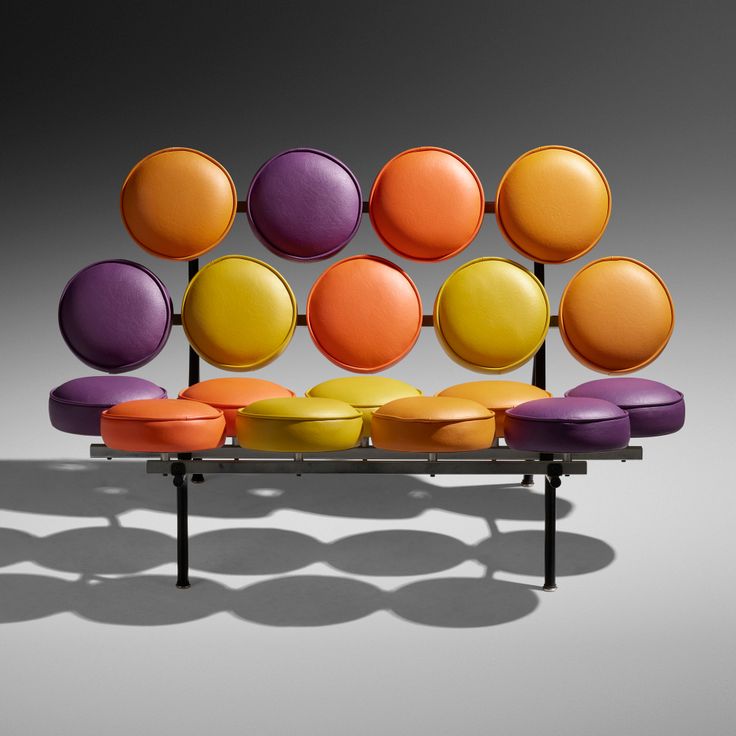 an orange, yellow and purple couch sitting on top of a metal stand with lots of round cushions