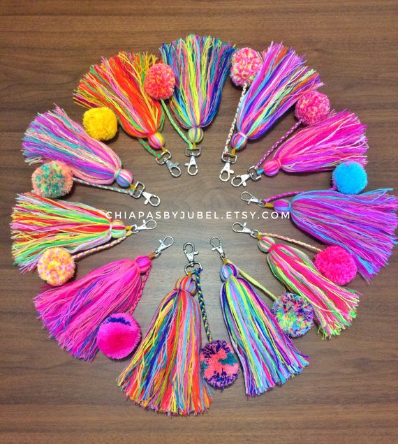 colorful tassel keychains arranged in a circle on a wooden surface with the words,