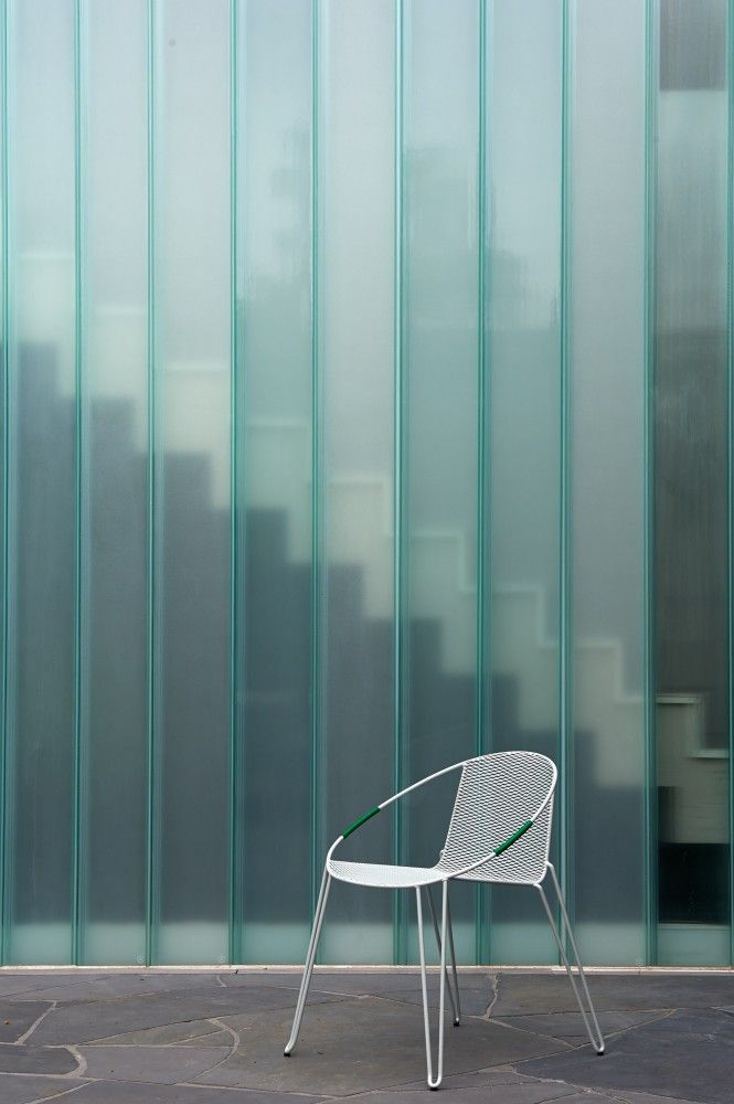 a white chair sitting in front of a green glass wall with vertical lines on it