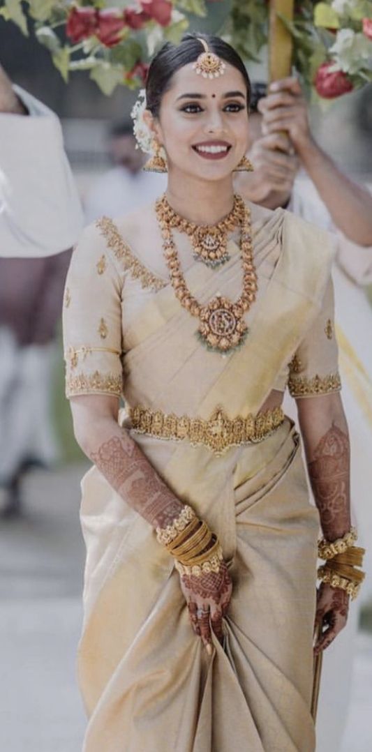 a woman in a white and gold sari walking down the street with flowers on her head