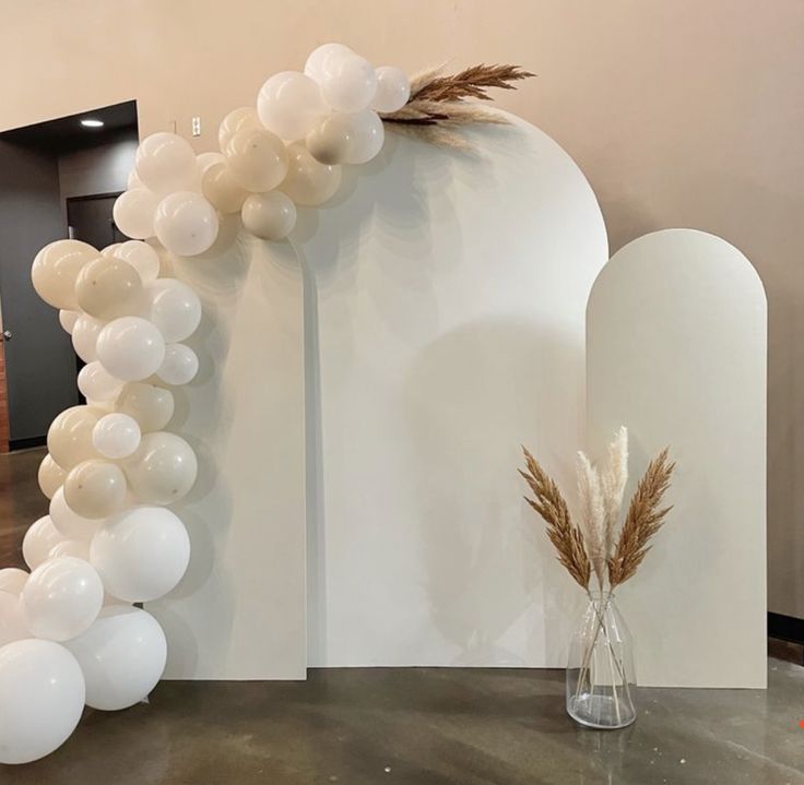 a vase filled with white balloons next to a tall balloon arch on a table in front of a wall