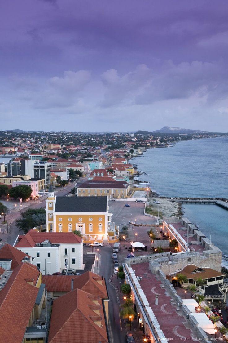 an aerial view of a city next to the ocean at night with lights on and buildings in the foreground