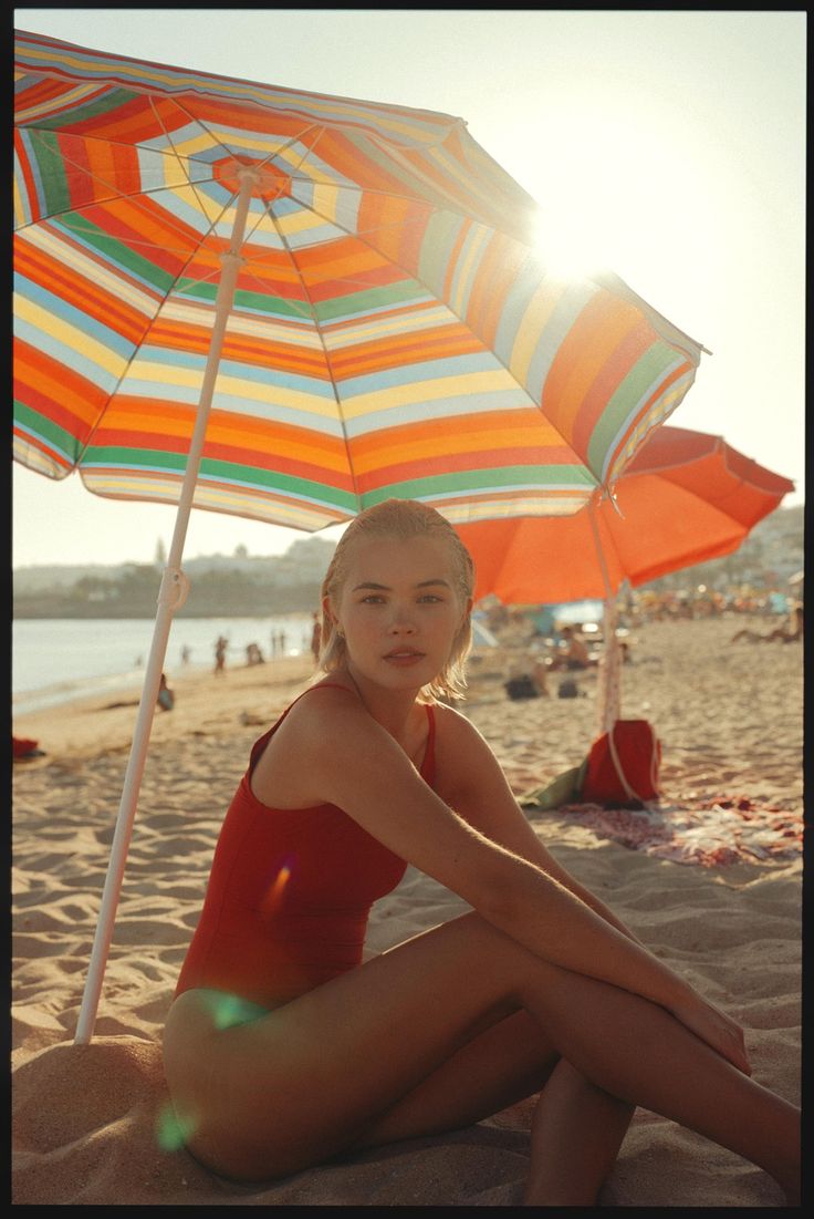 a woman sitting on the beach under an umbrella