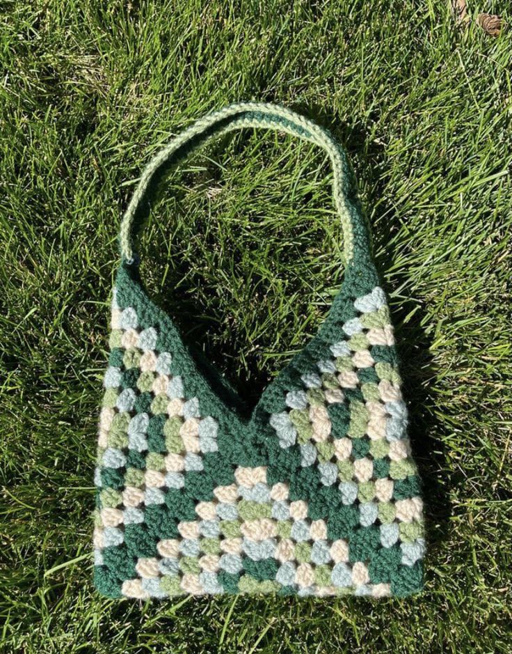 a crocheted bag sitting on top of green grass in the middle of a field